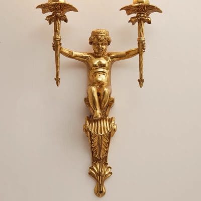 Ornamental gold wall sconce featuring a cherubic figure holding two candle holders, decorative and elegant design for luxury interior decor.