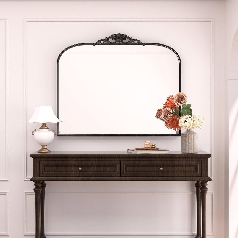 Elegant dark wood console table with a decorative mirror above, adorned with a white lamp and a vase of colorful flowers, perfect for a stylish optical store display.