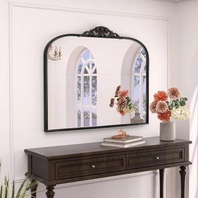 Elegant mirror with black ornate frame above a dark wooden console table decorated with colorful flowers and books in a stylish room setting.