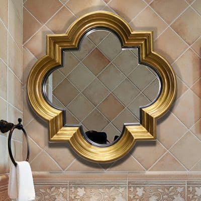 Intricate gold and black ornate wall mirror in a luxurious bathroom with beige tiled walls and floral patterned tile border, perfect for upscale home decor.