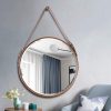 Reflective round mirror with leather strap hanging on modern bedroom wall, emphasizing stylish interior decor, aesthetic furniture, and contemporary home design.