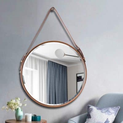 Reflective round mirror with leather strap hanging on modern bedroom wall, emphasizing stylish interior decor, aesthetic furniture, and contemporary home design.
