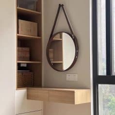 Mirror with leather strap hanging above wooden cabinet and wall outlet in modern interior.