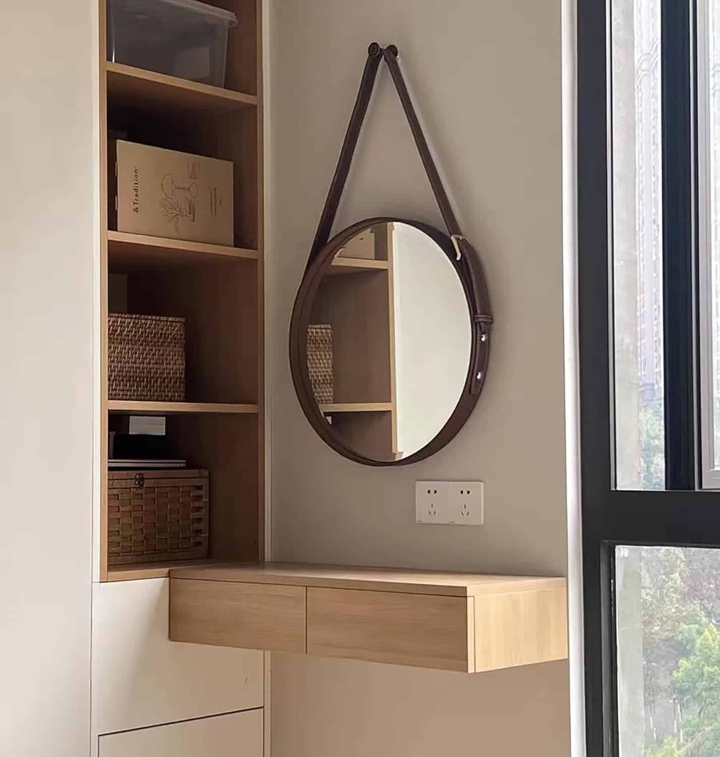Mirror with leather strap hanging above wooden cabinet and wall outlet in modern interior.