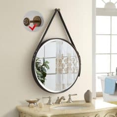 Vintage round mirror with leather strap, wall-mounted decor, bathroom vanity with elegant fixtures, and natural light in a bright, airy space.