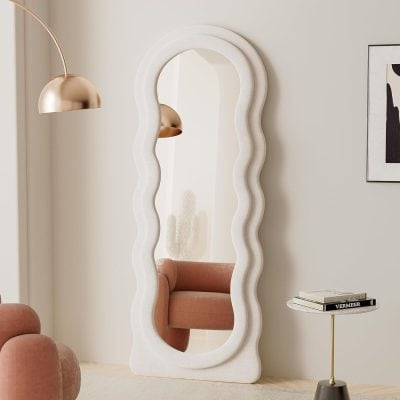 Wavy full-length mirror with white textured frame in modern interior decor.