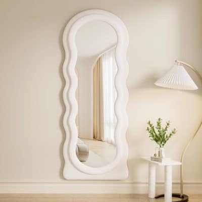 Reflective wavy-edge white mirror in modern interior with side table and table lamp.