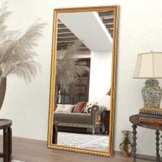 Elegant gold-framed full-length mirror reflecting stylish living room decor, including sofa, pillows, side table, and decorative vases, perfect for enhancing home interior aesthetics.