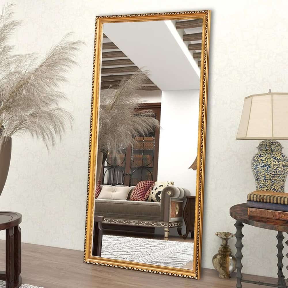 Elegant gold-framed full-length mirror reflecting stylish living room decor, including sofa, pillows, side table, and decorative vases, perfect for enhancing home interior aesthetics.