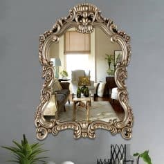 Intricate antique-style gold-framed mirror reflecting a stylish living room decorated with modern and vintage furniture, greenery, and natural light. Perfect for enhancing elegant home decor.