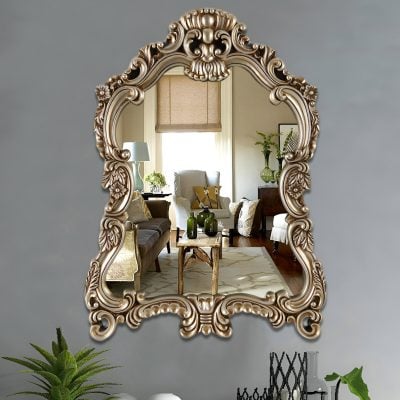 Intricate antique-style gold-framed mirror reflecting a stylish living room decorated with modern and vintage furniture, greenery, and natural light. Perfect for enhancing elegant home decor.
