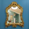 Ornate gold baroque mirror with floral details hanging on vibrant blue wall, elegant decor, luxurious interior design accessory, stylish home decoration, Monalisa Medical store ambiance.