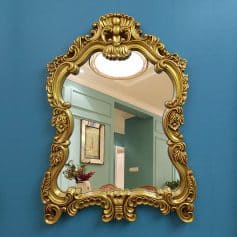 Ornate gold baroque mirror with floral details hanging on vibrant blue wall, elegant decor, luxurious interior design accessory, stylish home decoration, Monalisa Medical store ambiance.