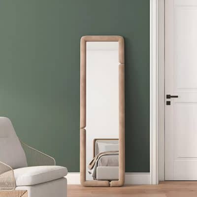Full-length beige cushioned frame mirror with rounded edges leaning against green wall in modern bedroom setting.