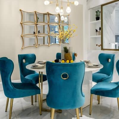 Blue velvet dining chairs around a white marble table with lemon decor and yellow floral centerpiece in an elegant, modern interior space.