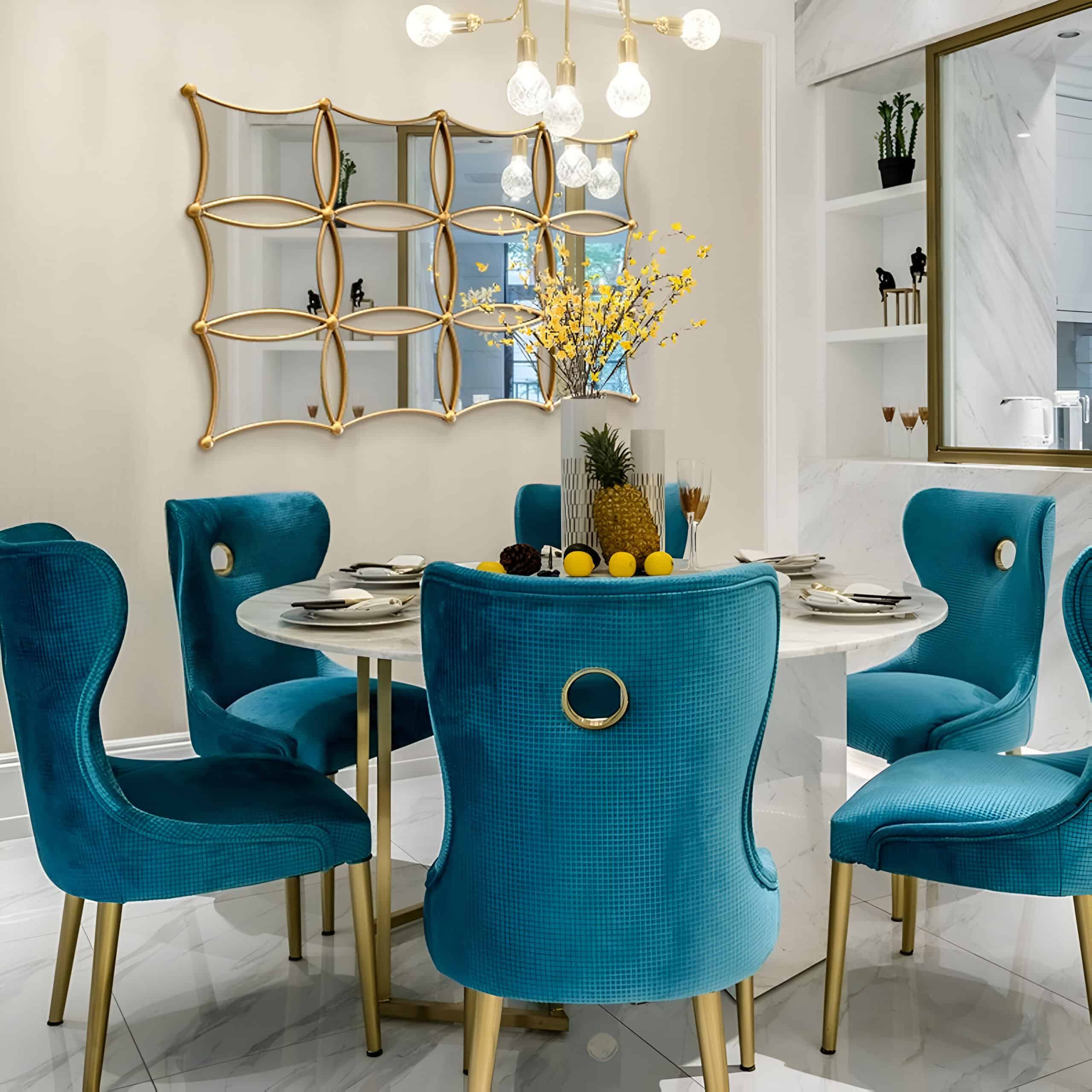 Blue velvet dining chairs around a white marble table with lemon decor and yellow floral centerpiece in an elegant, modern interior space.