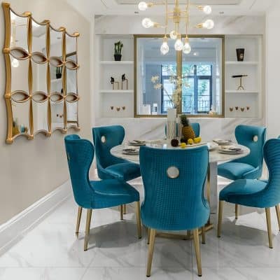 Blue upholstered dining chairs with gold accents surrounding a white marble table in a modern, elegant dining area at Monalisa Store.