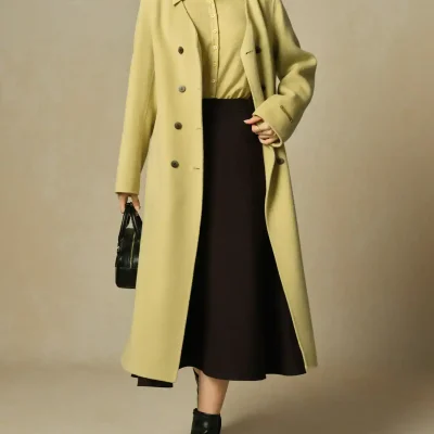 Elegant women's fashion ensemble featuring a long beige coat layered over a matching beige top, paired with a black midi skirt, ankle boots, and stylish accessories, perfect for stylish and professional looks.