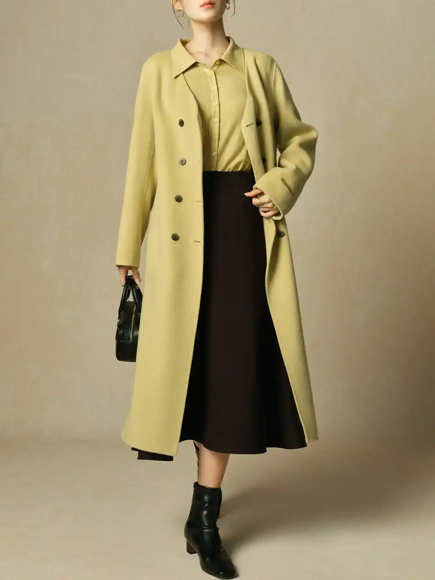 Elegant women's fashion ensemble featuring a long beige coat layered over a matching beige top, paired with a black midi skirt, ankle boots, and stylish accessories, perfect for stylish and professional looks.