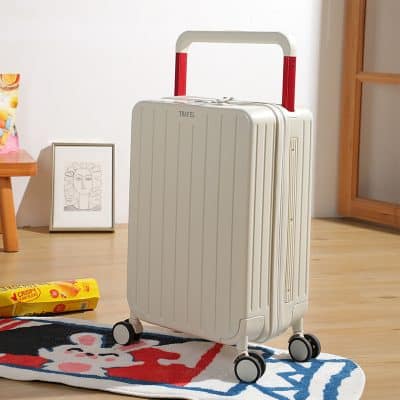 Hard-shell white travel suitcase with red accents and four wheels on a colorful rug in a modern home interior.