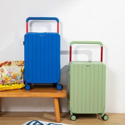Blue travel suitcases with red and green handles on wooden table at home.
