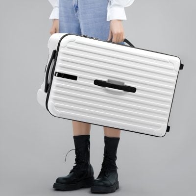 Removable white suitcase with black accents, designed for travel, held by a person in casual denim and boots, emphasizing stylish and functional luggage for modern travelers.