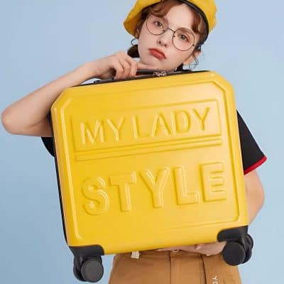 Stylish young woman holding yellow suitcase with