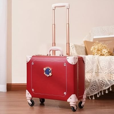 Pink suitcase with floral embellishment and extendable handle, ideal for travel and kids, displayed in a cozy home with lace-covered furniture and flowers, combining style and practicality.
