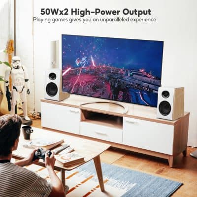 High-power wireless speakers on a modern entertainment center with a curved TV displaying a sci-fi game scene, in a cozy living room setup.