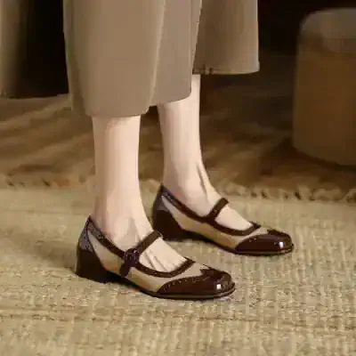 Mary Jane style black and beige shoes with a strap and low heel on a woman standing on a carpeted floor.