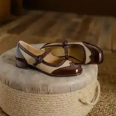 Vintage women's brown and beige Mary Jane shoes with decorative straps, placed on a round fabric-covered ottoman for stylish display.