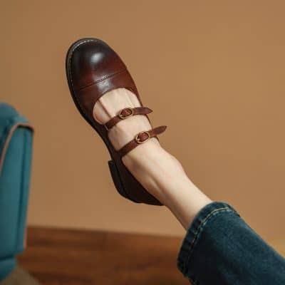 Brown leather Mary Jane shoes with double straps and gold buckles, stylish and comfortable footwear option, perfect for casual or professional settings.