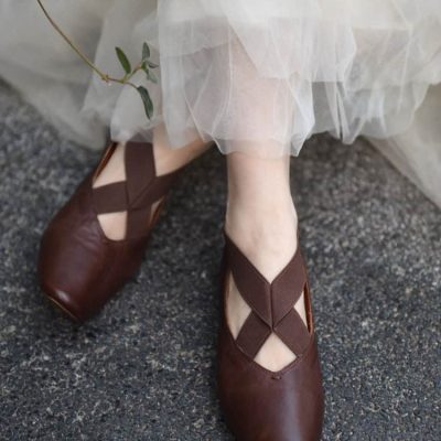 Brown leather Mary Jane shoes with crisscross straps, paired with a white sheer skirt, showcasing elegant footwear fashion for women.
