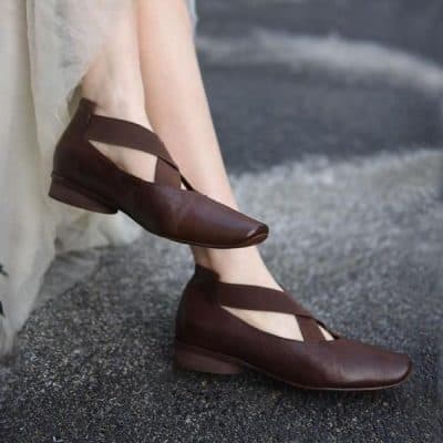Traditional brown leather dance shoes with crisscross straps on a dark textured surface. Perfect for performance or casual wear, combining style and comfort.