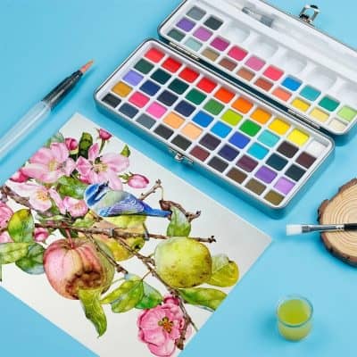 Bright watercolor paint set with pink blossoms, a detailed watercolor painting of a bird, and art supplies on a light blue background for creative artistic expression.