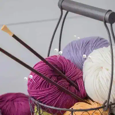 Soft multi-colored yarn balls, knitting needles, and crochet hooks in a wire basket, ideal for knitting and crochet enthusiasts at Monalisa Store for quality knitting supplies.