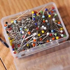 Colored sewing pins in a plastic container for medical or accessory purposes, suitable for textile and craft projects.