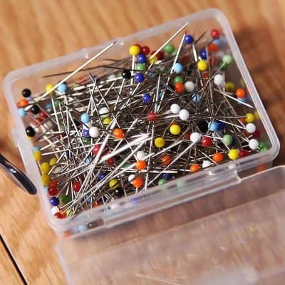 Colored sewing pins in a plastic container for medical or accessory purposes, suitable for textile and craft projects.