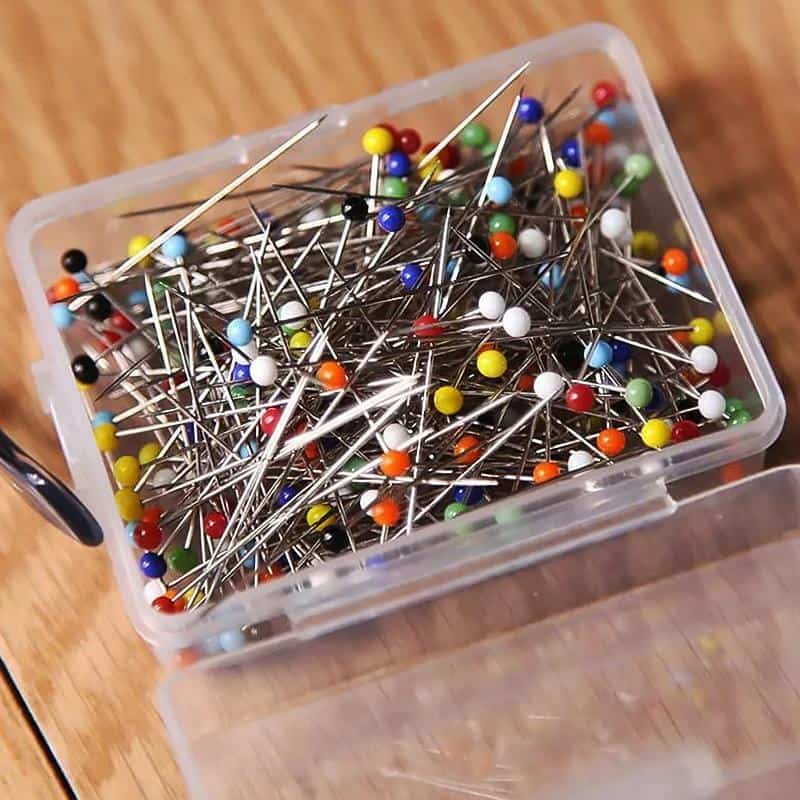 Colored sewing pins in a plastic container for medical or accessory purposes, suitable for textile and craft projects.