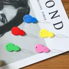 Colorful whale-shaped sewing pins for fashion and textile design, assorted in blue, red, yellow, green, and pink, featured on a Monalisa Store magazine cover with a black and white portrait.