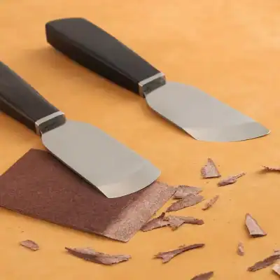 Sharp knives with black handles and stainless steel blades on a wooden surface, used for cutting leather or similar materials.