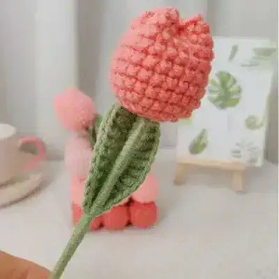 Pink crochet flower pen with green leaf decorative accessory, perfect for stationery or gift use. Handmade, soft-textured design enhances aesthetic appeal for desk decor or creative projects.