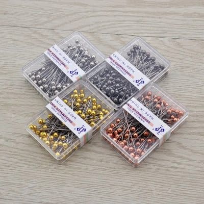 Shiny gold, silver, black, and rose gold colored dressmaking pins in transparent plastic containers for sewing and tailoring crafts.