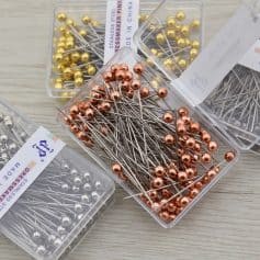 Stainless steel dressmaker pins in rose gold, gold, and silver, organized in clear plastic containers, ideal for sewing, tailoring, and embroidery projects.