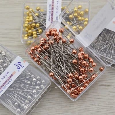 Stainless steel dressmaker pins in rose gold, gold, and silver, organized in clear plastic containers, ideal for sewing, tailoring, and embroidery projects.