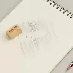 Eraser on lined notebook page with faint text, spiral-bound notebook, pink mechanical pencil, office stationery, clean workspace.