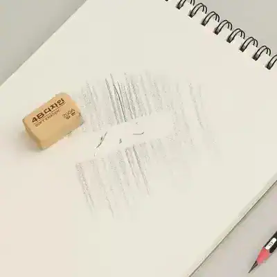 Eraser on lined notebook page with faint text, spiral-bound notebook, pink mechanical pencil, office stationery, clean workspace.