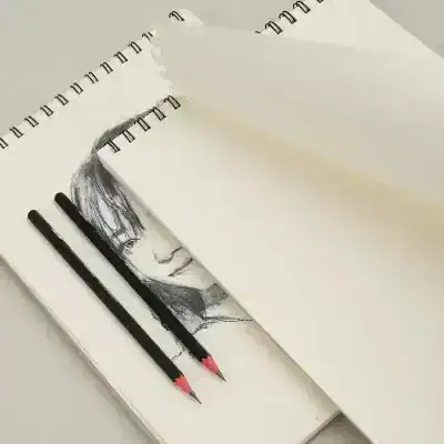 Sketched portrait of a woman on sketchbook pages with black pencils, illustrating detailed eye and facial features, perfect for art enthusiasts and portrait artists.