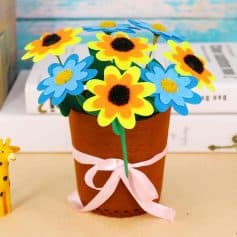 Flowers craft, colorful paper daffodils and blue flowers in a brown paper pot with pink ribbon, decorative floral arrangement for gift or home decor.