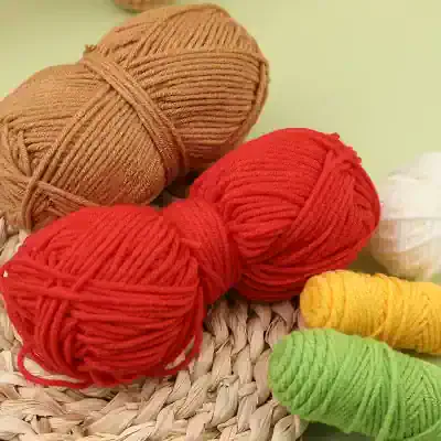 Brown, red, yellow, white, and green yarn skeins for knitting or crochet projects, displayed on a woven surface. Perfect for creating warm winter accessories like scarves, hats, and sweaters.